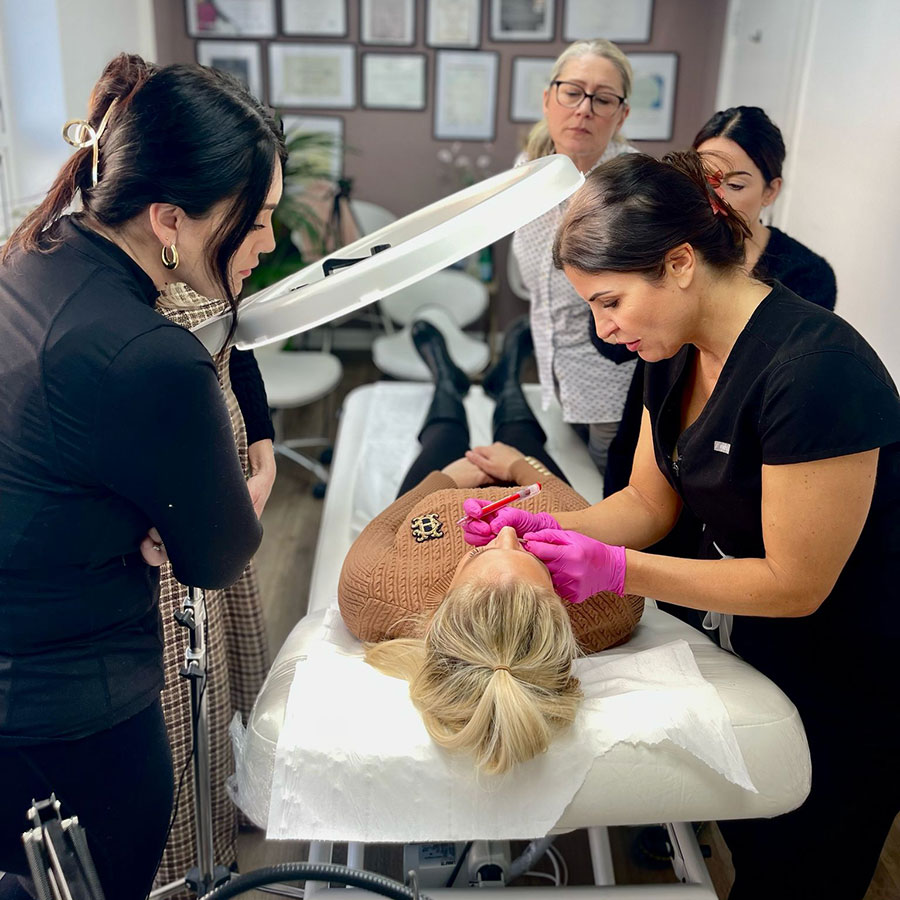 Tutor demonstrating a treatment on a client while students watch during a PMU Skool training day